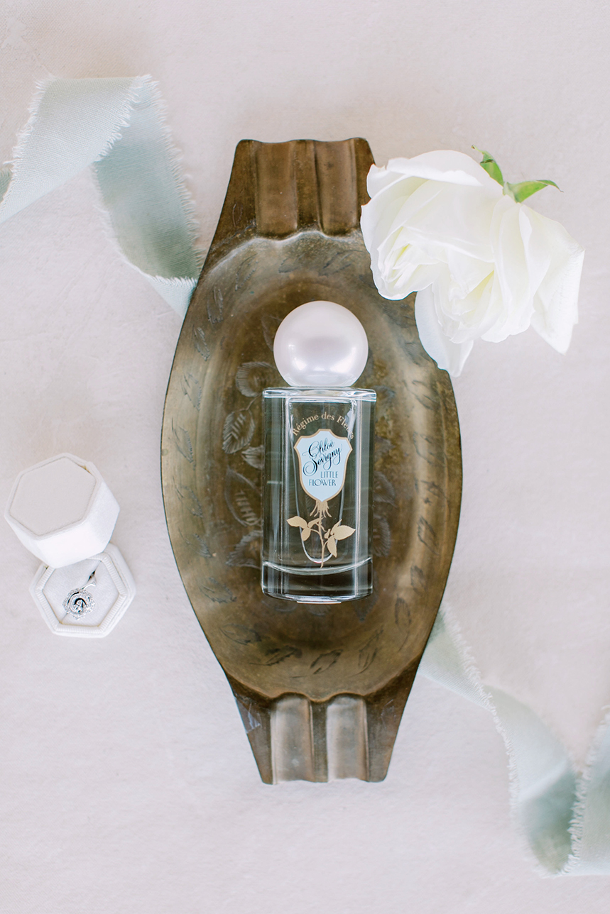 Flat lay of perfume sitting on antique silver platter with a diamond ring and white rose