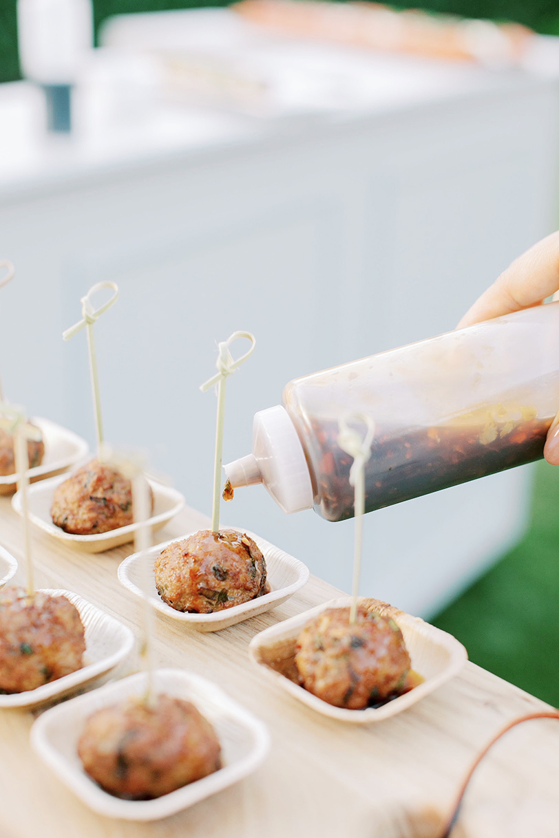 Drizzling chili garlic soy sauce on Asian meatballs in individual bamboo vessels.