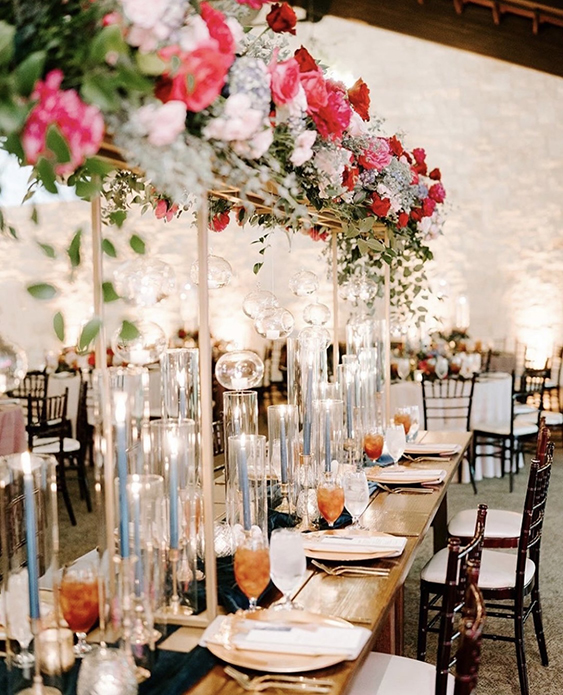 Tall centerpieces with florals in differing shades of pinks dangling down on candlelight and beautiful place settings