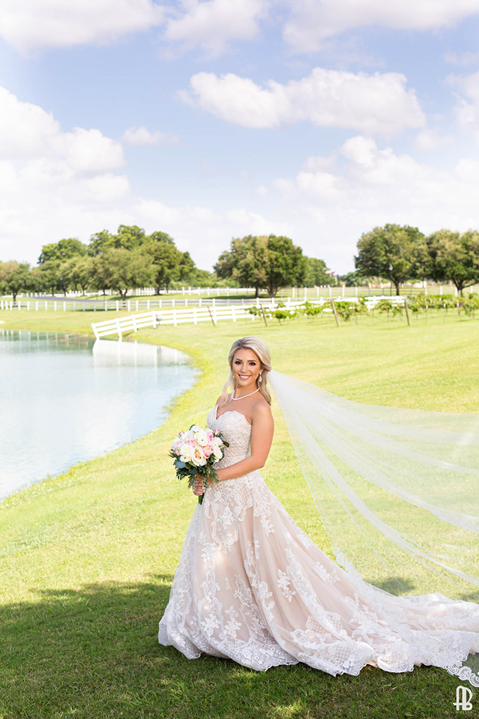 Portrait Photo of a Bride holding her bouquet standing in front of a lake with green pastures.