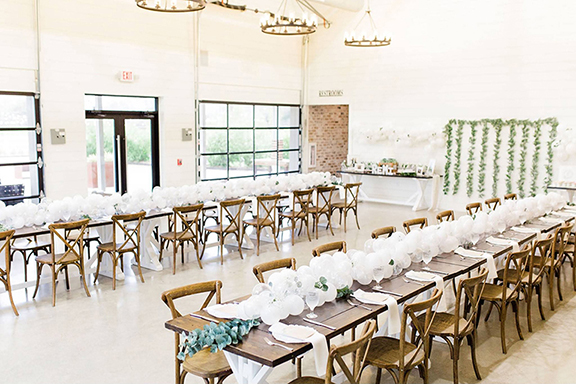 Interior photo of The Barn at Briscoe Manor. Farm tables are decorated with white balloons and greenery.