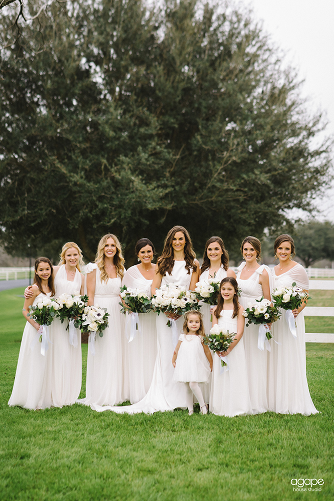 Bride and bridal party dressed in white standing in front of large tree.