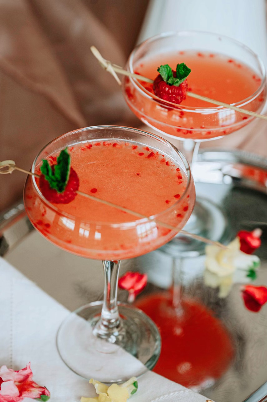 Bright peach colored cocktails with strawberry garnish in coupe glasses