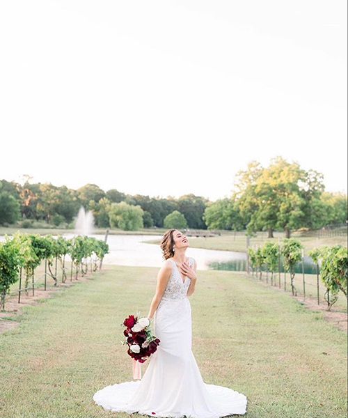 Bride standing in the middle of a vineyard holding her bouquet with a view of the lake behind her